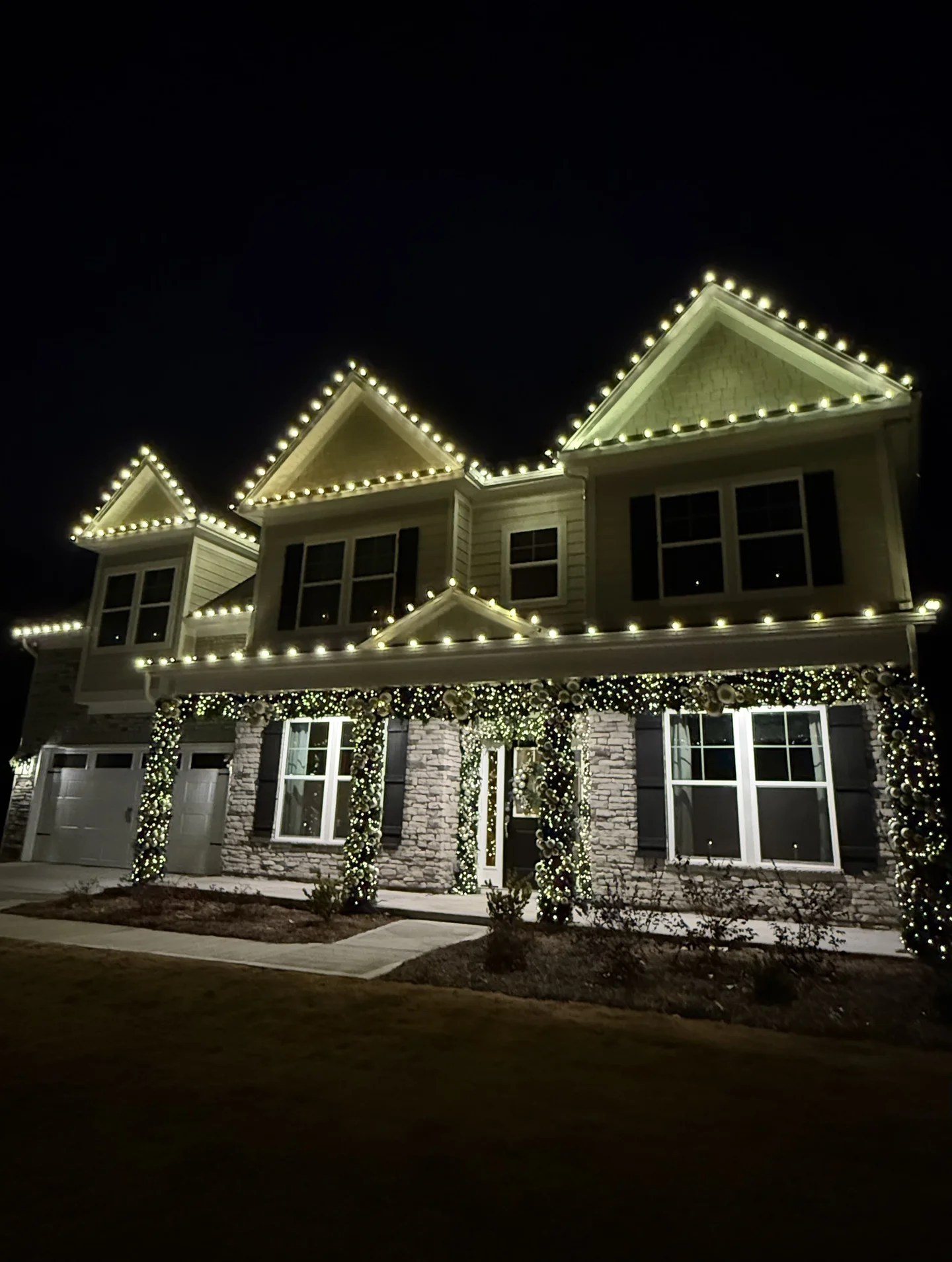 Home outlined with warm white Christmas roofline lights and illuminated porch garland at night