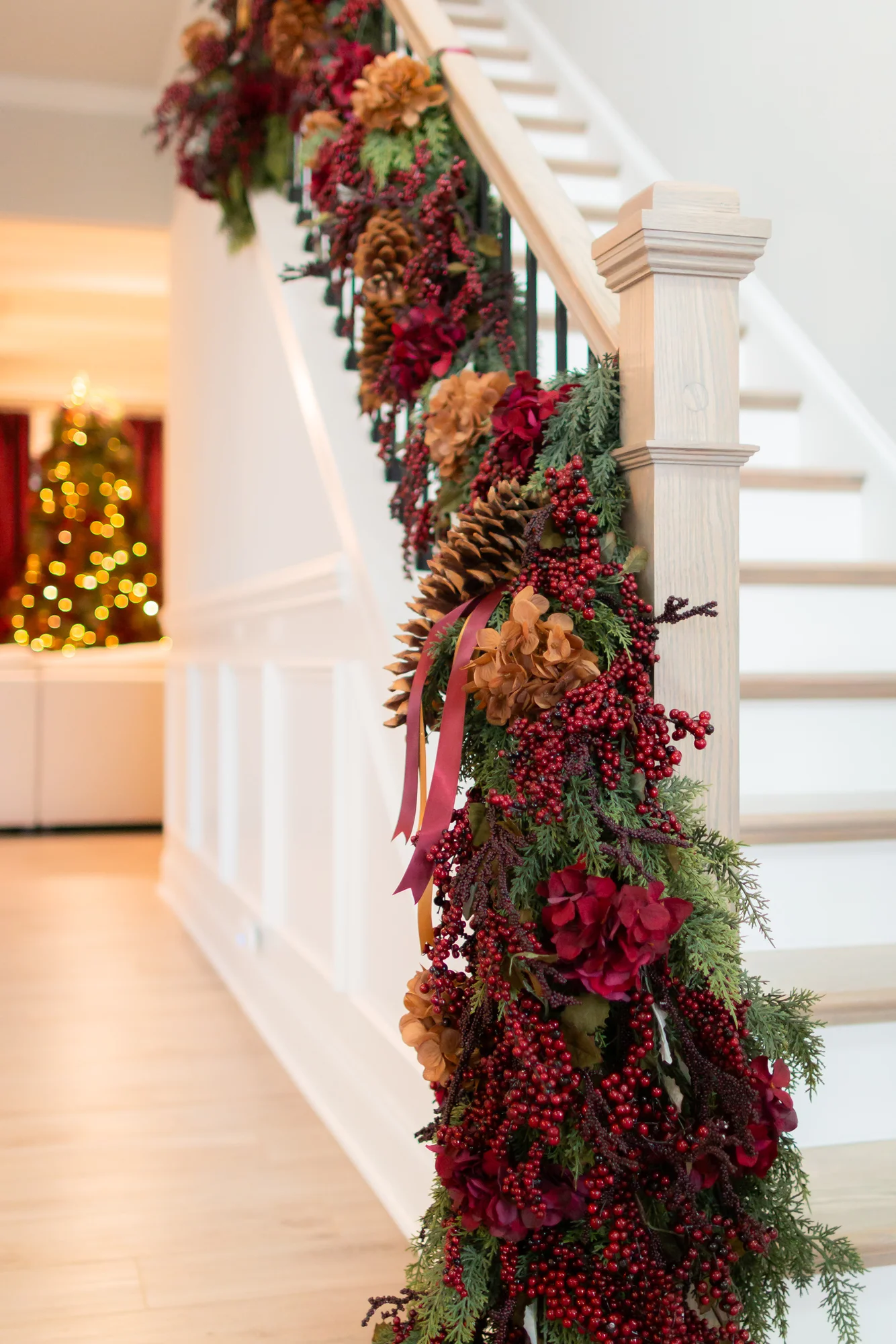 White staircase railing styled with burgundy ribbon, red berries, pinecones, and evergreen garland